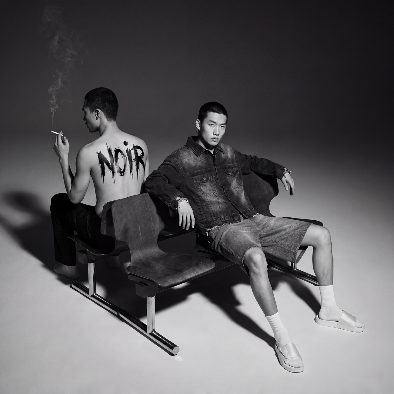 NOIR 2026 Lookbook — two models on a bench, NOIR painted on the back